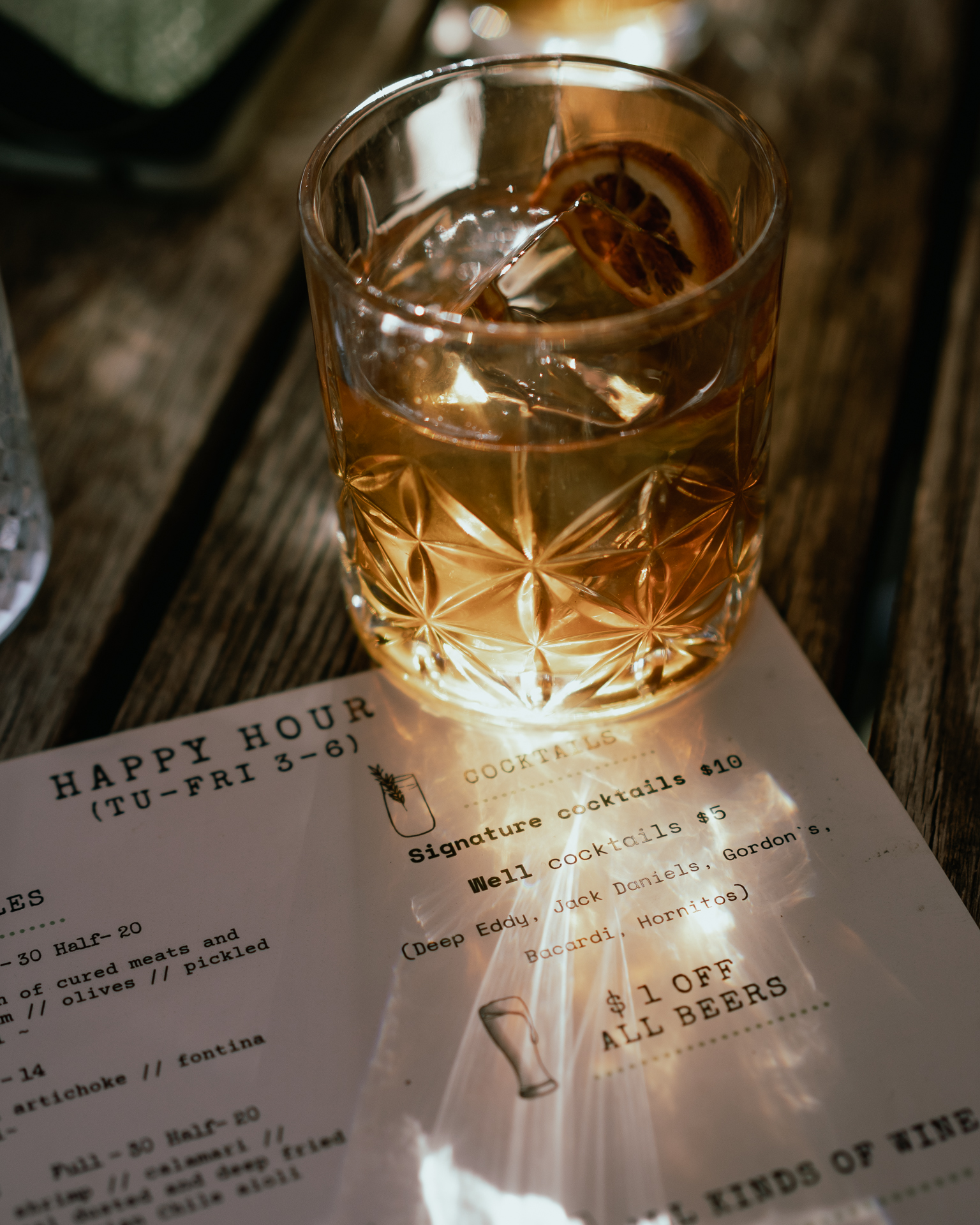 Featured Image: A whiskey cocktail refracts setting sunlight onto a bar menu.